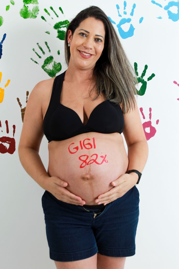 Portrait of a pregnant woman smiling with painted belly and colorful handprint background.